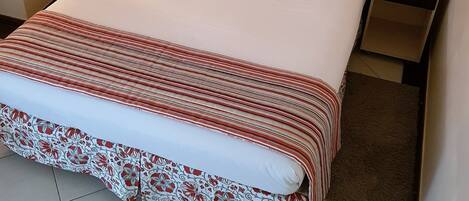 Una cama bien tendida con ropa de cama estampada con motivos florales, una mesita de noche con un control remoto y un cuadro en la pared.