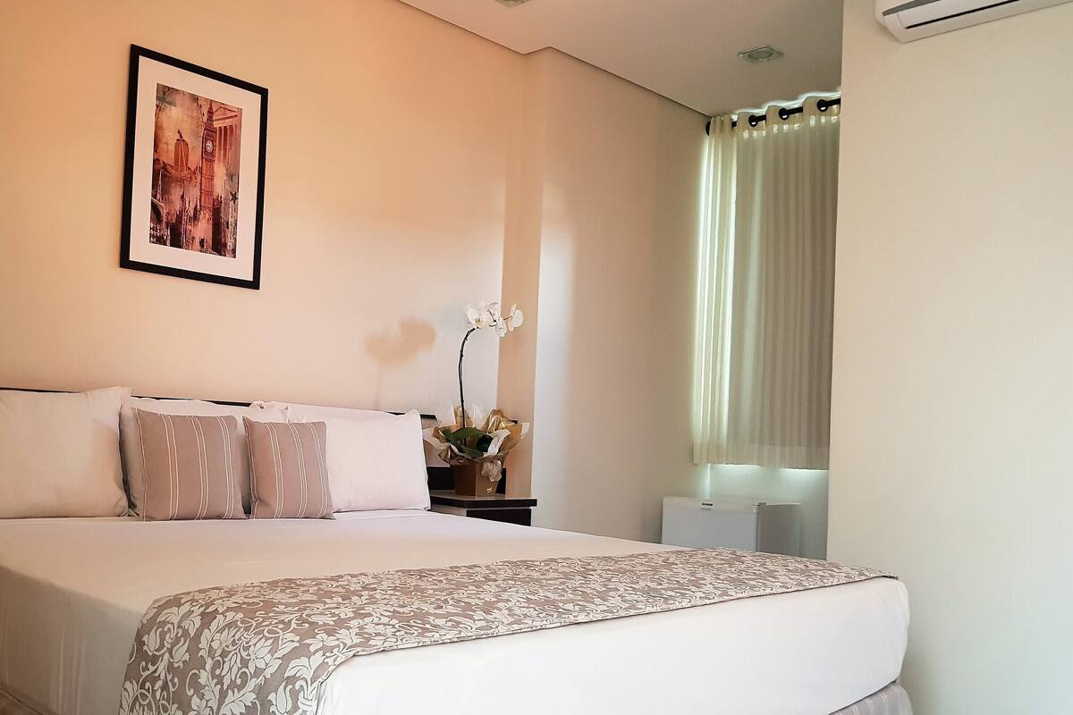 A neatly made bed with a patterned bedspread, a framed picture on the wall, and a potted orchid on a bedside table.