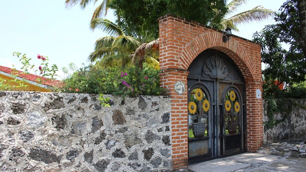 Un muro de piedra con un arco de ladrillo que conduce a una puerta, adornada con girasoles.