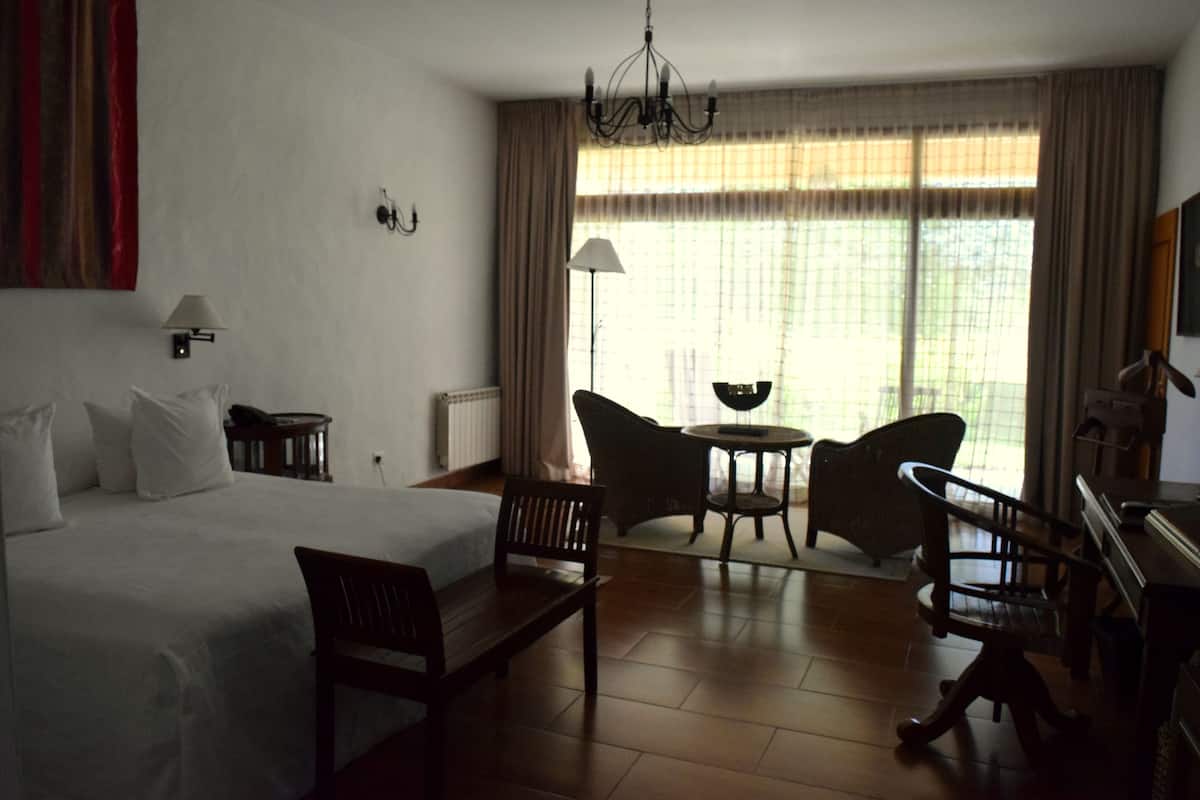 A hotel room with a large bed, two chairs, a small table, a desk, and a window with curtains.