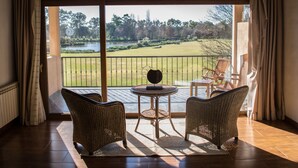 A room with a large sliding glass door leading to a view of a golf course and a lake. Inside, there are wicker chairs and a small table with a decorative item.
