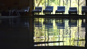 An indoor swimming pool with lounge chairs and a view of trees through the window.