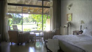 A hotel room with a bed, two armchairs, a small table, and a view of the outdoors.
