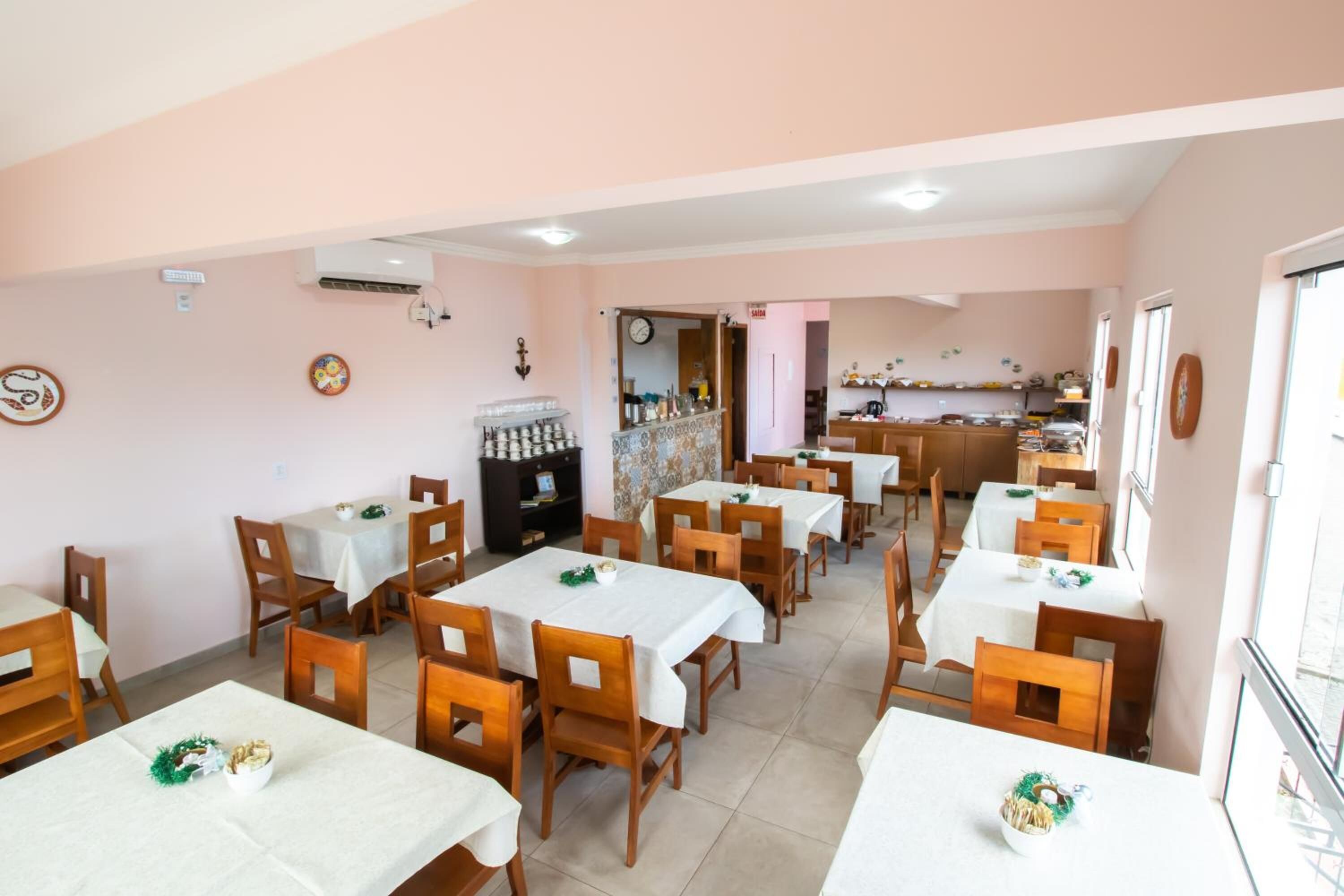 Un espace repas avec plusieurs tables et chaises, une cuisine à l’arrière-plan et une horloge au mur.