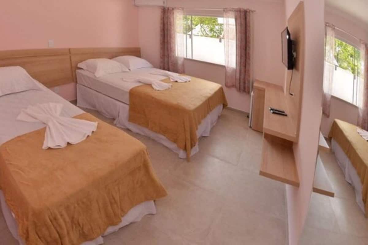 A hotel room with two beds, a TV mounted on the wall, and a window with curtains.