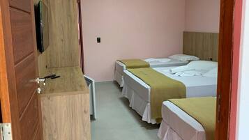A hotel room with three beds, a wooden wardrobe, a television, and a small table.