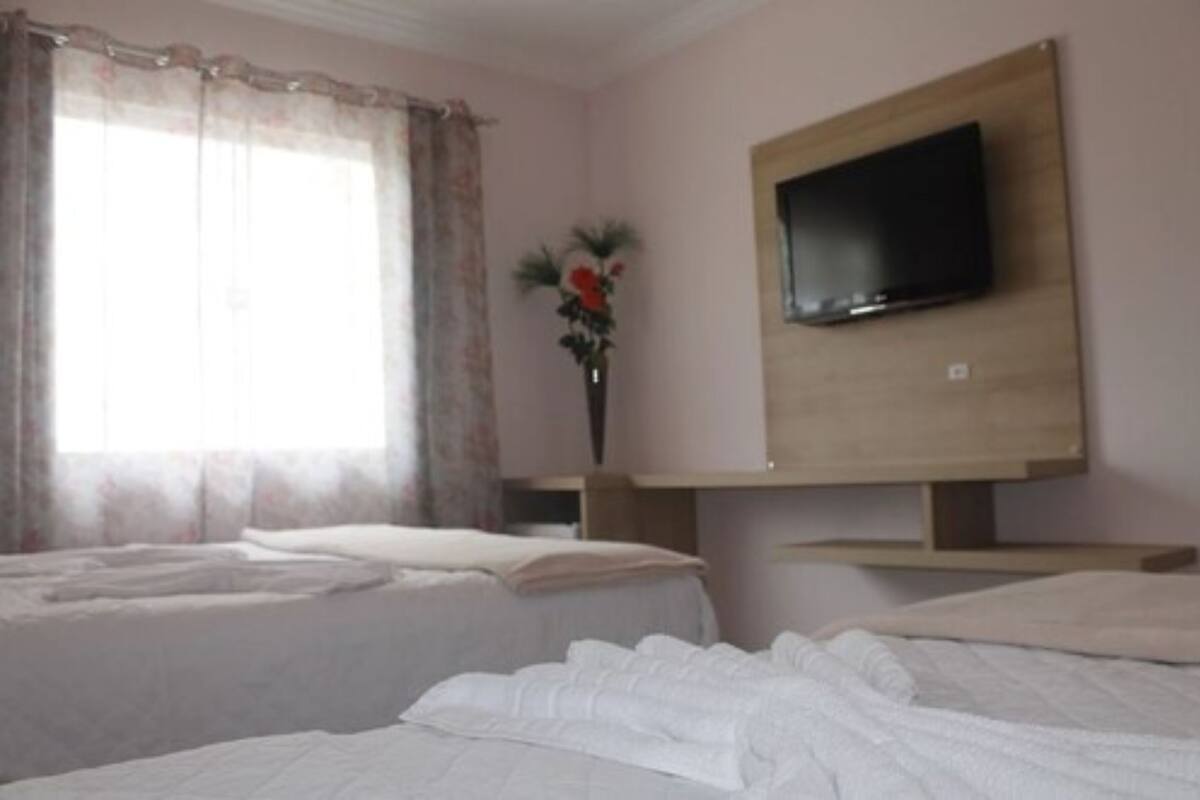 A hotel room with two beds, a TV mounted on the wall, and a window with curtains.