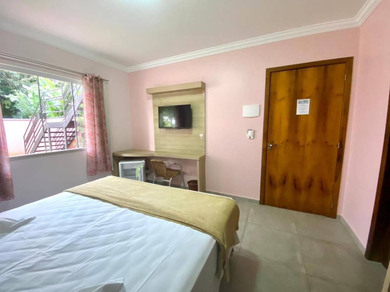 A hotel room with a bed, a desk, a television, and a door.