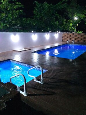 An outdoor swimming pool at night with a wooden deck and a brick wall in the background. - Pousada Baía dos Açores (Penha)