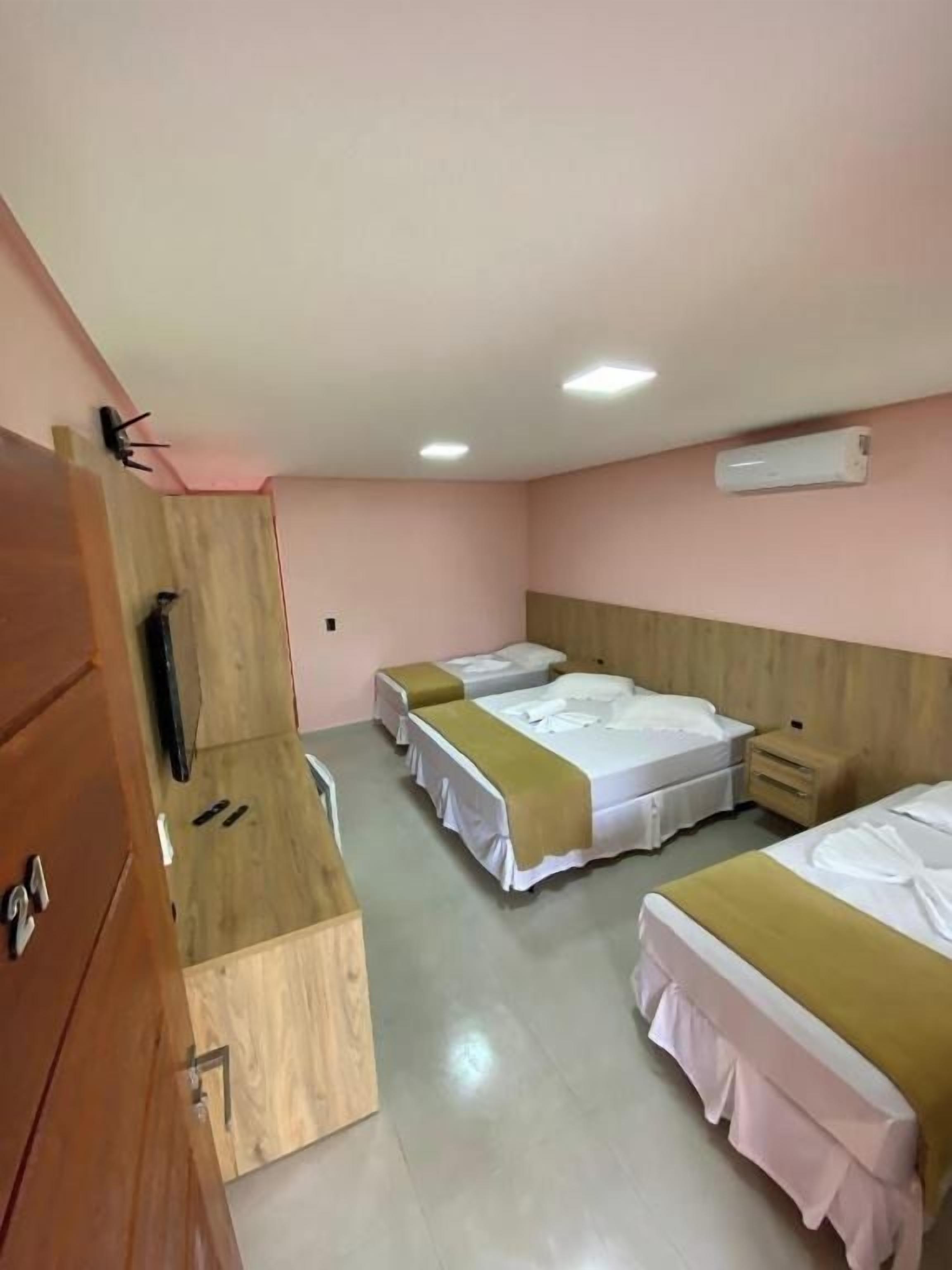 A hotel room with two beds, a wooden wardrobe, a desk, and a wall-mounted air conditioner.