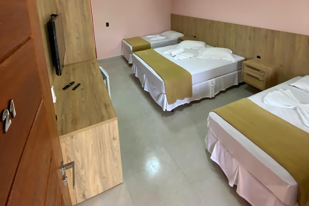 A hotel room with three beds, a wooden desk, a television, and an air conditioning unit.