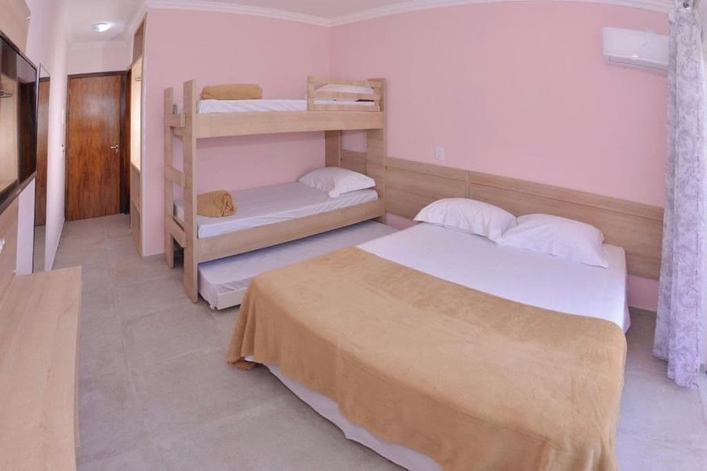 A bunk bed room with a single bed, a wooden desk, and a door in the background.