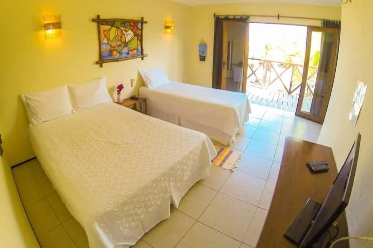 A hotel room with two beds, a television, and a balcony with a wooden railing.