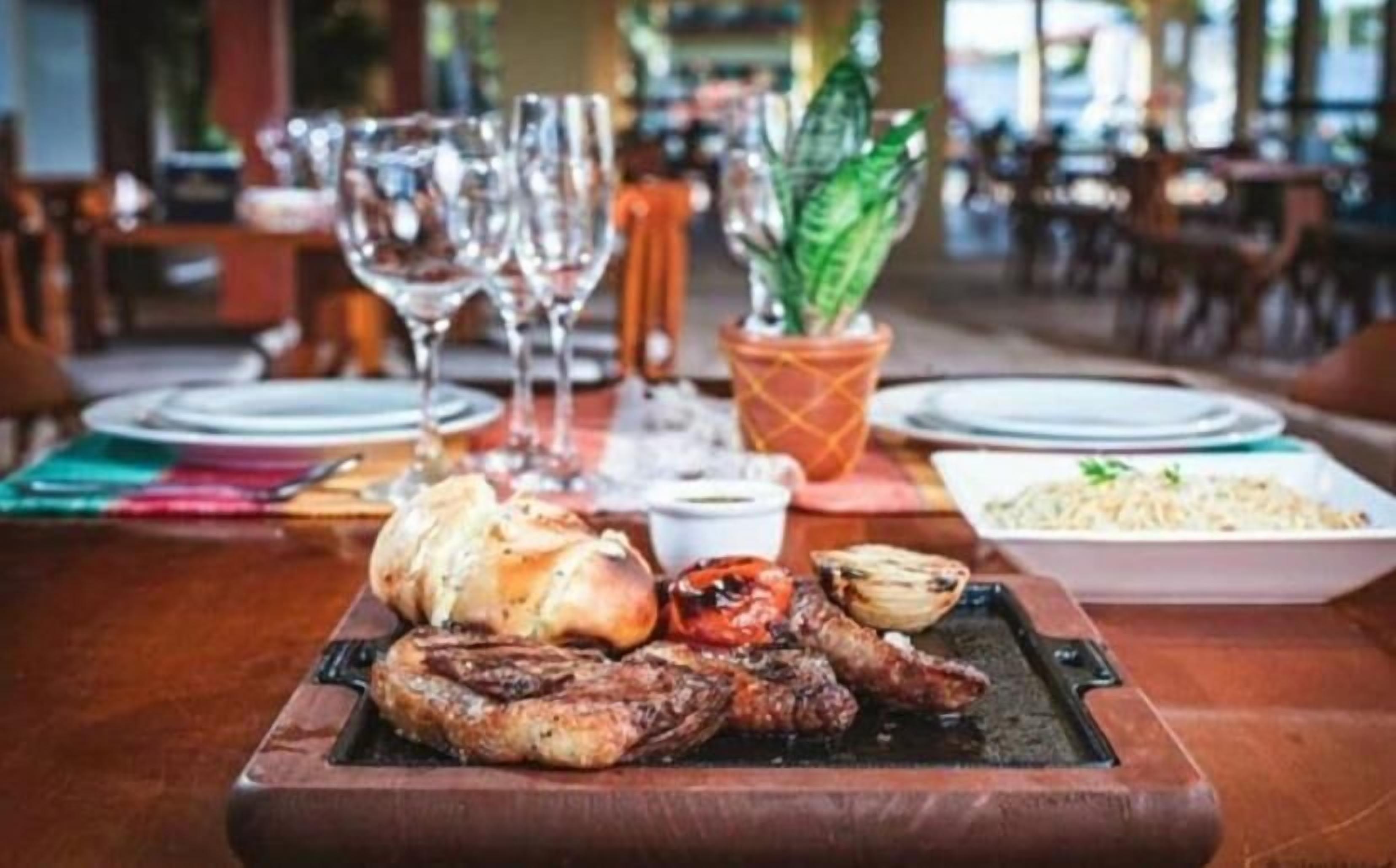 A dining table with a variety of grilled meats, a bowl of pasta, and a potted plant.