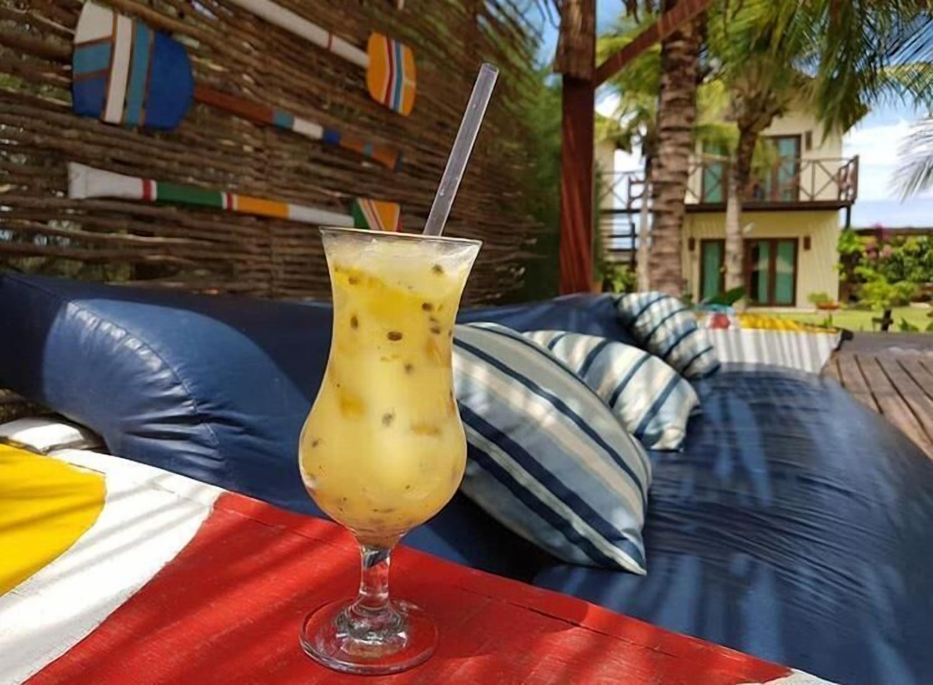 A tropical setting with a glass of a yellow beverage on a red tablecloth, a blue sofa with striped pillows, and a wooden deck.