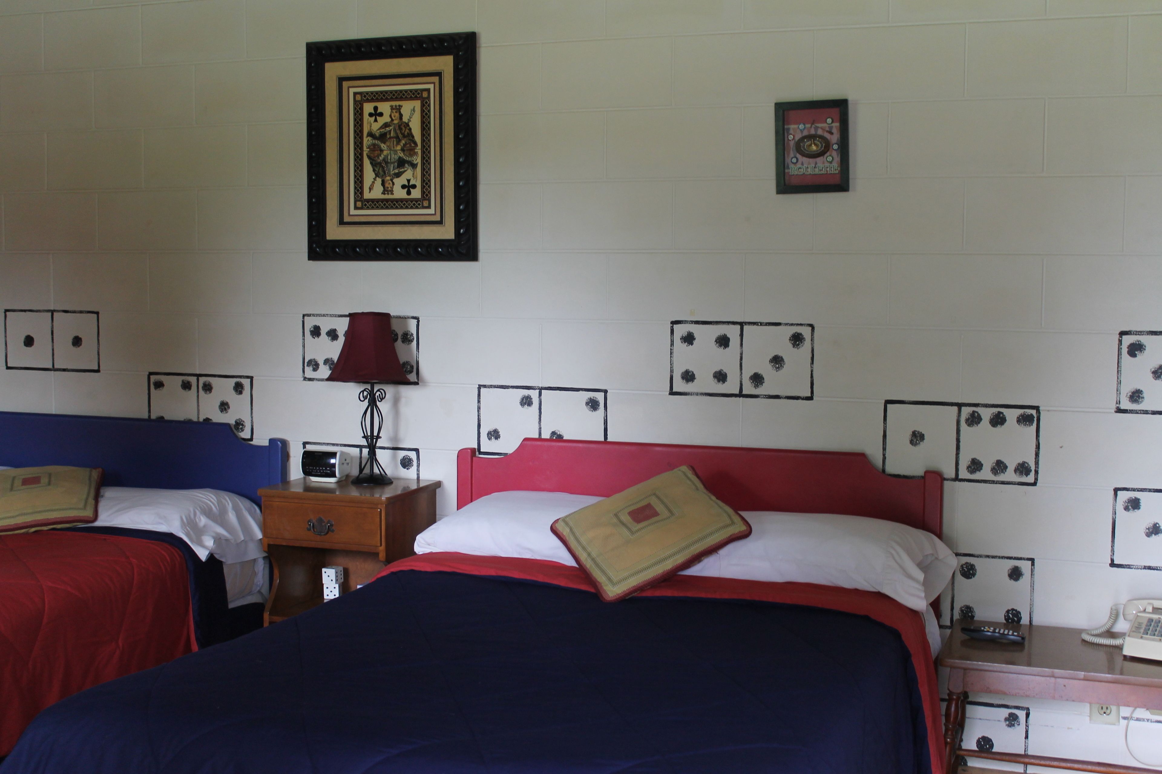 Habitación de hotel con dos camas, una mesita de noche con lámpara, teléfono y adornos en la pared, incluyendo fotografías enmarcadas.