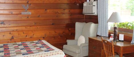 Acogedora habitación tipo cabaña con pared de madera, cama acolchada, una silla, un escritorio y ventana con cortinas.