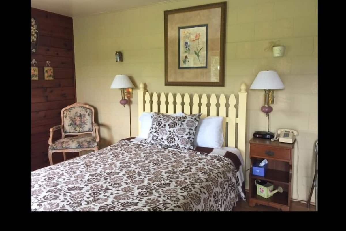 A bedroom with a bed, two bedside lamps, a chair, a nightstand, and a wall-mounted telephone.