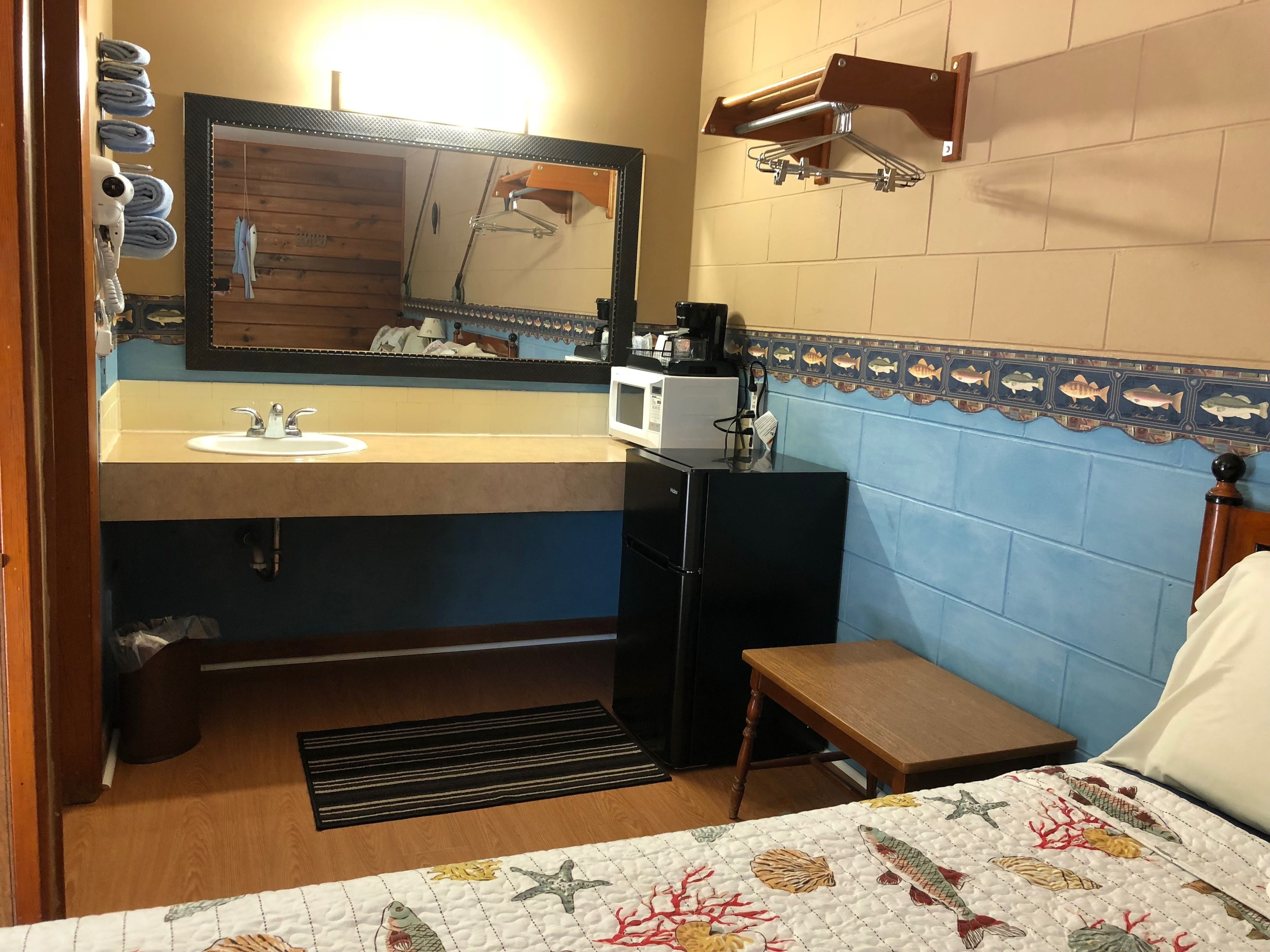 Habitación de hotel compacta con lavamanos, espejo, microondas y una pequeña mesa.