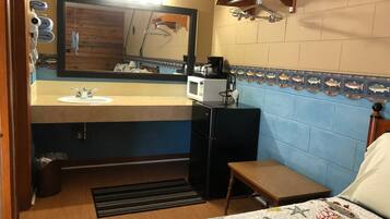 Habitación de hotel compacta con lavamanos, espejo, microondas y una pequeña mesa.