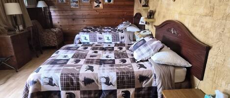 A room with a wooden floor, a bed with a checkered bedspread, a wooden headboard, a nightstand with a lamp, and a wall-mounted clock.