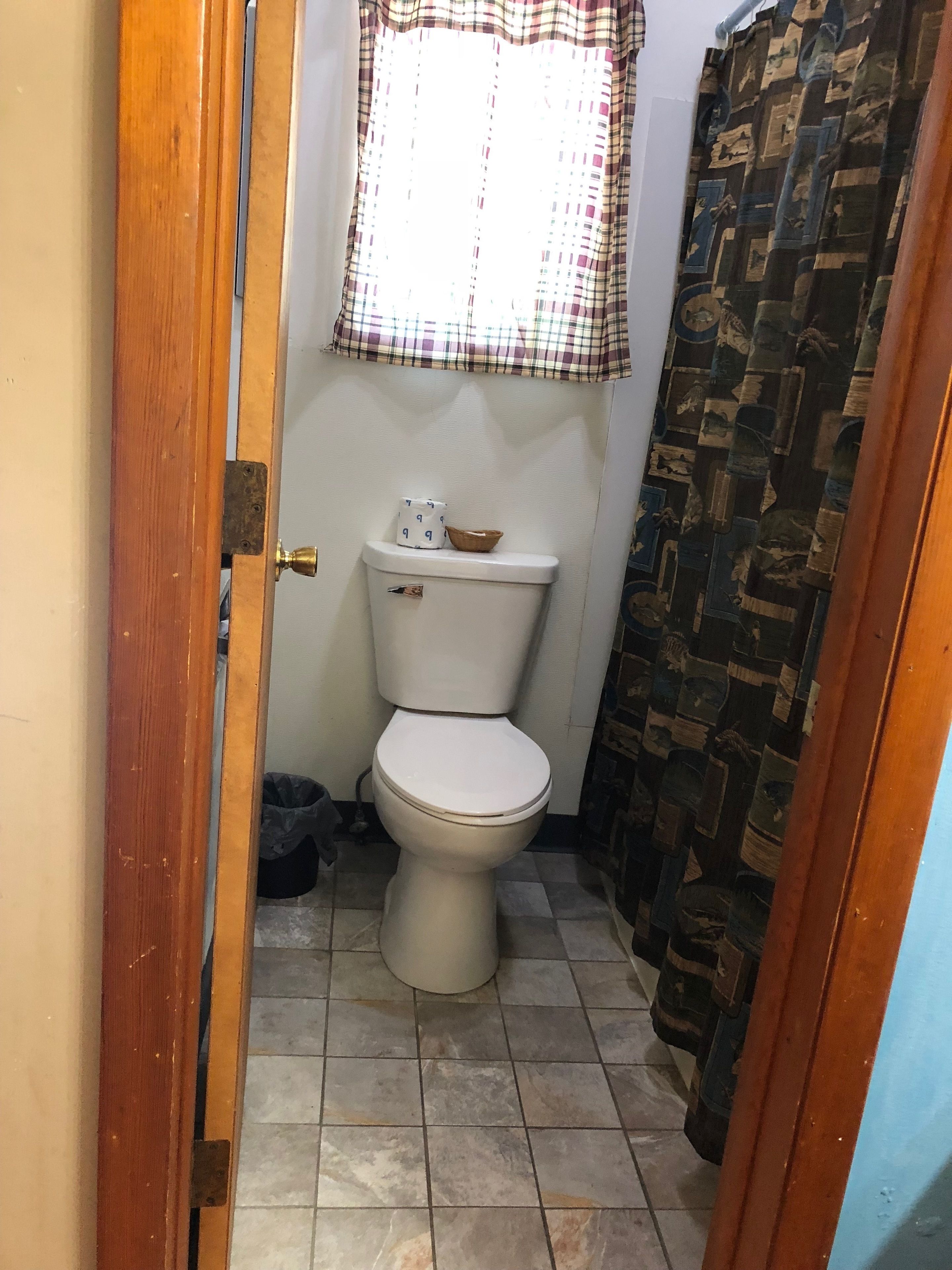 Un baño pequeño con inodoro, una ventana con cortina a cuadros y una cortina de ducha con diseño estampado.