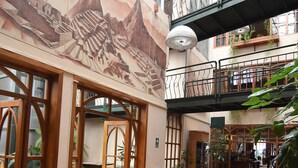 Un grand espace intérieur doté de plusieurs tables et chaises, d’une fresque murale et d’un balcon agrémenté de plantes.