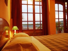 Una habitación de hotel con un ventanal grande, una cama y una mesita de noche con lámpara.