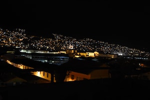 Vista nocturna de una ciudad densamente poblada con edificios iluminados y una colina destacada con una estructura en forma de cúpula.