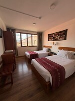 Una camera d'albergo con due letti, mobili in legno, una scrivania, una sedia, una finestra con tende e un'opera d'arte appesa al muro.