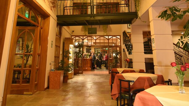 Un restaurant à plusieurs niveaux, doté d’un escalier central, de tables recouvertes de nappes orange et de plantes en pot.