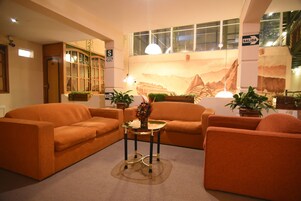 Una sala de estar con sofás naranja, una mesa de centro de vidrio y plantas en macetas.