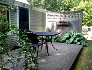 A patio with a table and chairs, a wooden deck, and a garden area with plants. - Morning Glory Inn (York)