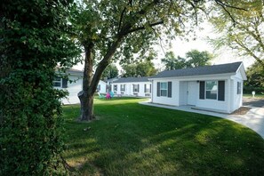 A row of white mobile homes with a grassy yard and a large tree in the foreground.