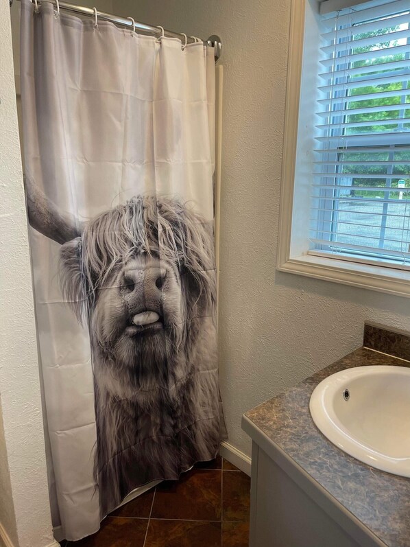 A bathroom with a shower curtain featuring a large animal print, a sink, and a window with blinds.
