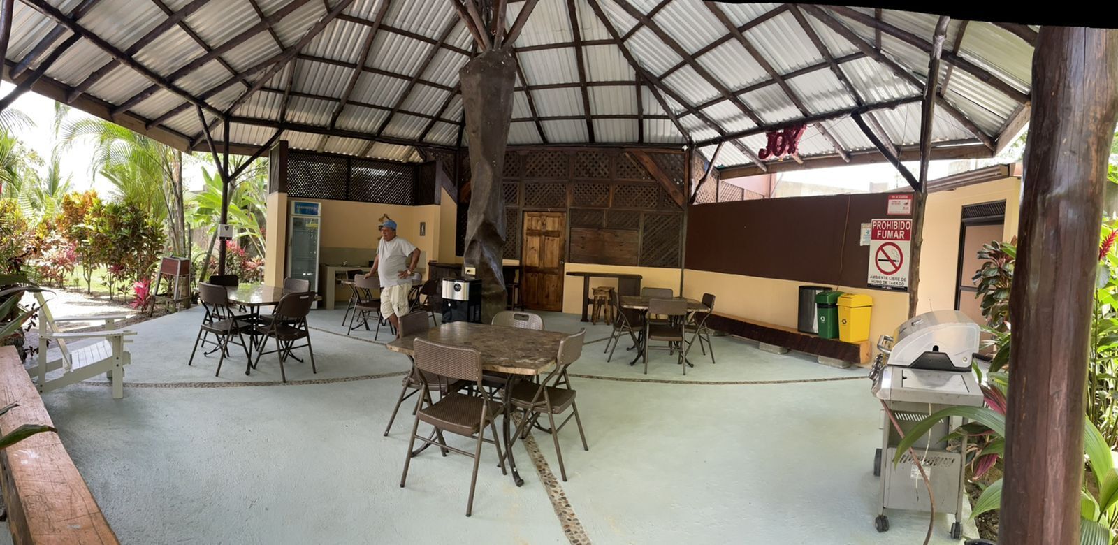 An outdoor covered dining area with tables and chairs, a grill, and a sign prohibiting smoking.