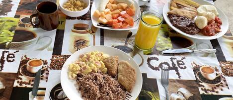 A table set with breakfast items including eggs, rice, bread, and fruit.