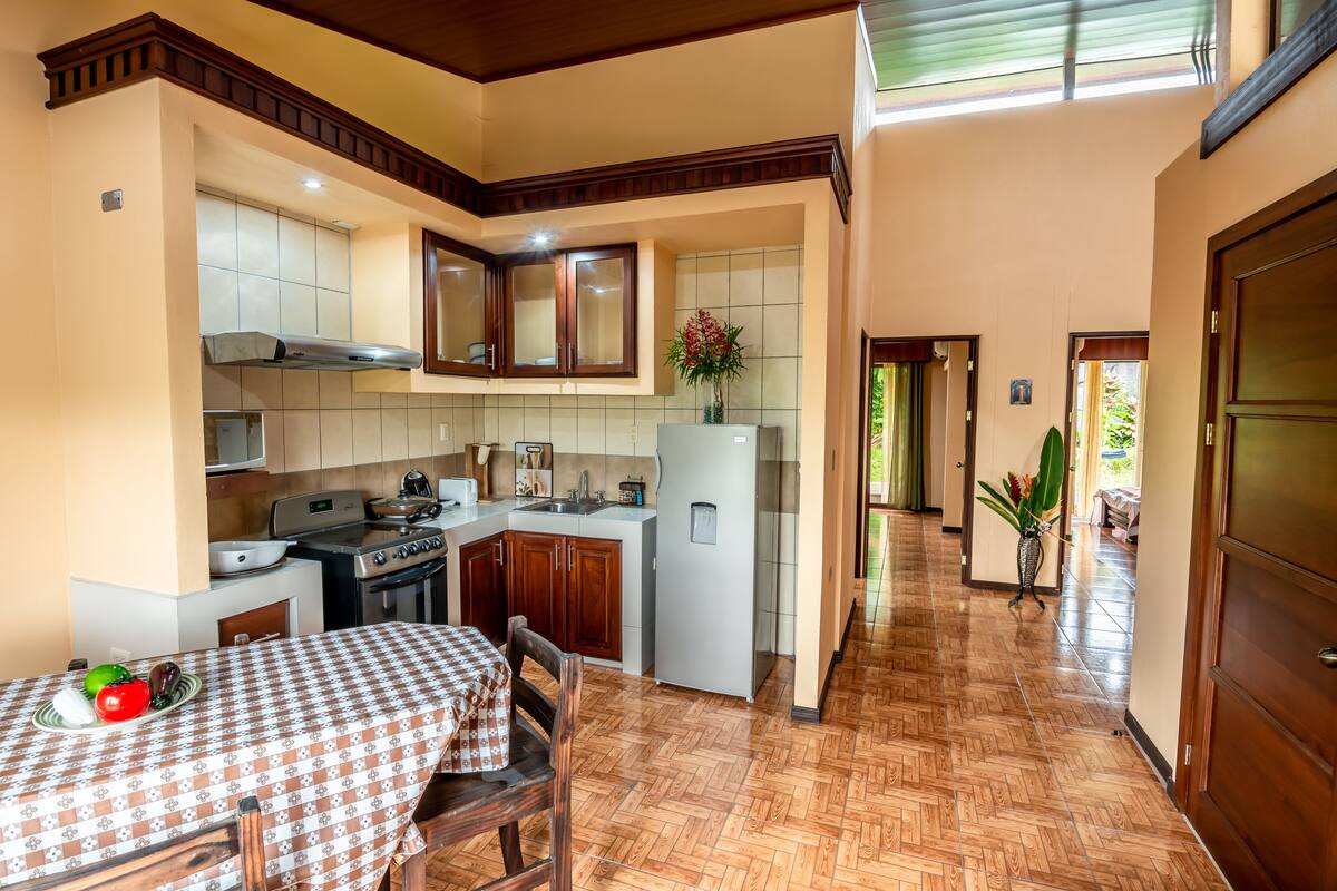 A compact kitchen with a dining area, featuring a checkered tablecloth, wooden cabinets, and a tiled backsplash.
