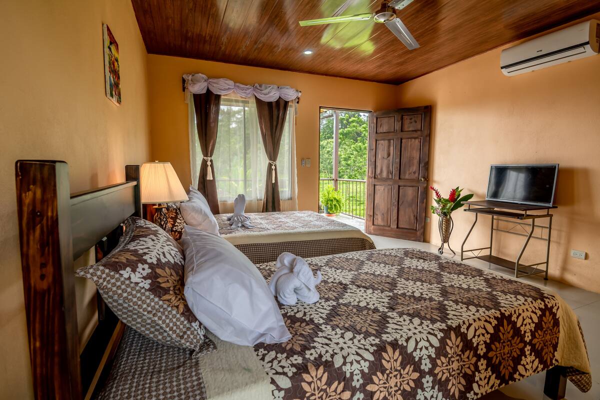A hotel room with two beds, a TV, and a balcony with curtains.