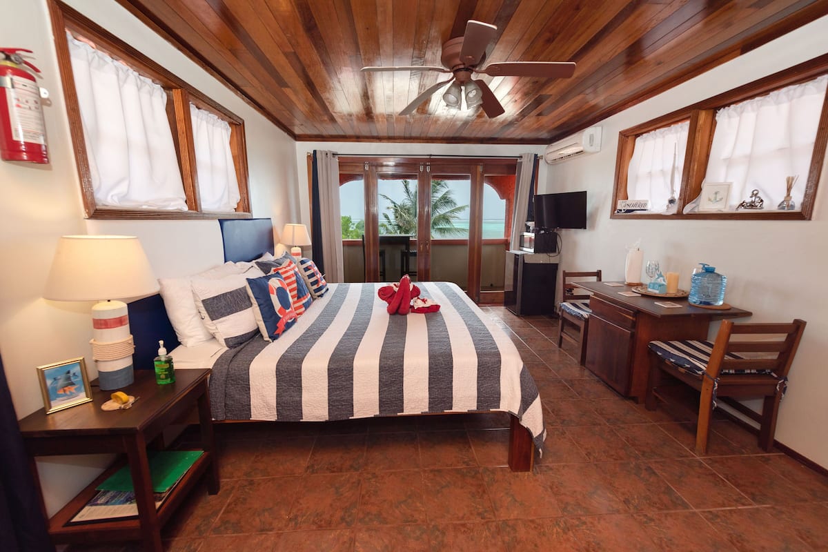 A hotel room with a bed, a desk, a chair, a television, and a window with a view of palm trees.