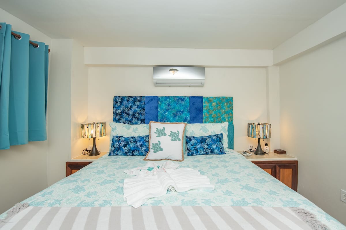 A neatly made bed with a patterned bedspread, two bedside lamps, and a wall-mounted air conditioner.