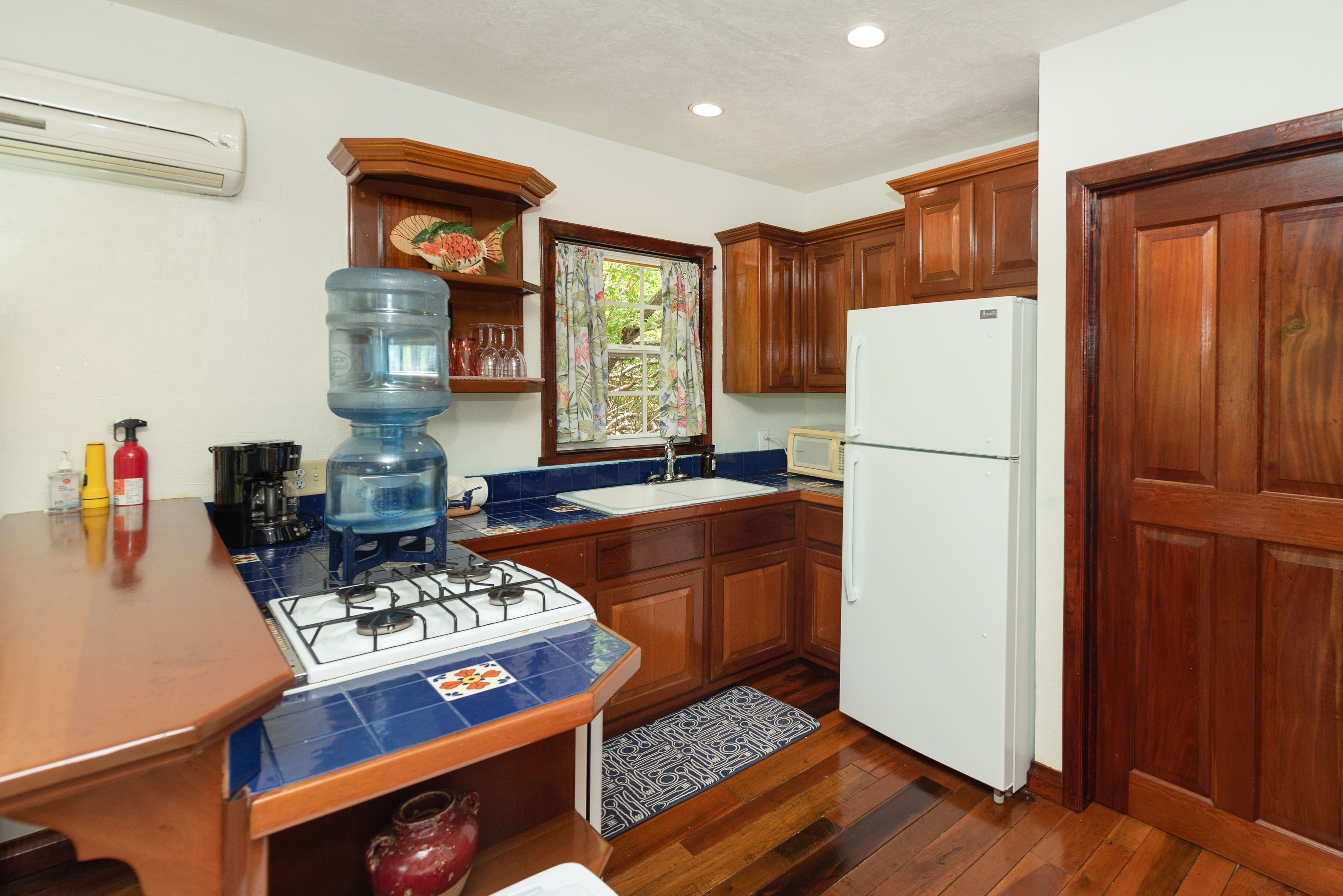 A compact kitchen with wooden cabinets, a white refrigerator, a gas stove, and a water dispenser.