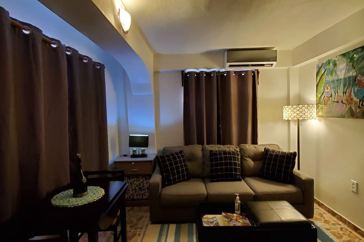A living room with a sofa, a coffee table, a lamp, a TV, and curtains.