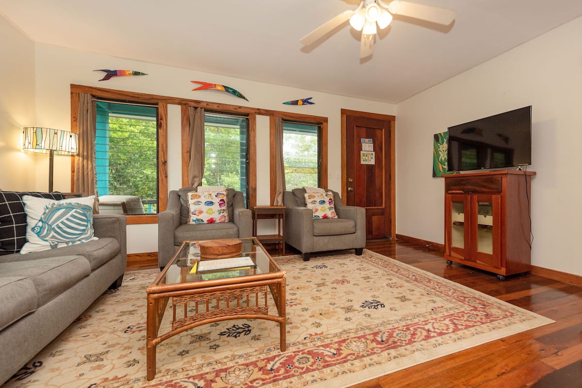 A living room with a sofa, two armchairs, a coffee table, a TV, and a ceiling fan.