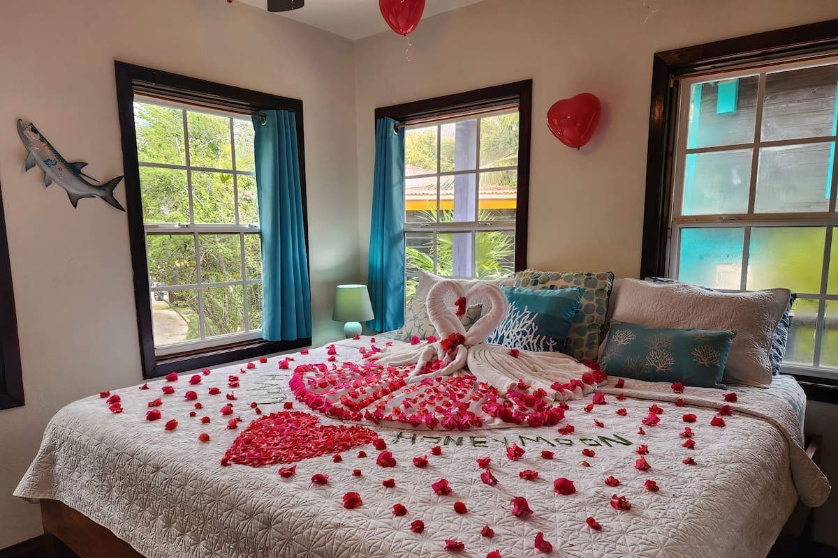 A bedroom with a bed adorned with rose petals and a swan-shaped decoration.