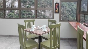 A conservatory with a table set for four, surrounded by green chairs, and large windows offering a view of a forested hillside. - Inka Tower (Machu Picchu)