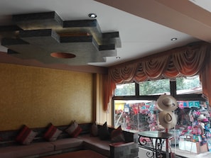 Een modern interieur met een modulaire bank, een decoratief plafond en uitzicht op een kleurrijke markt door een groot raam.