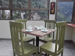 Een eetgedeelte met een tafel voor vier personen, stoelen en een raam met uitzicht op een bebost gebergte.