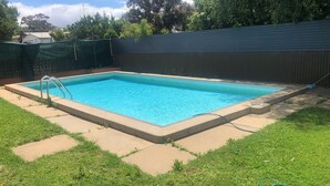 Una piscina rectangular con una escalera en un lateral, rodeada por un solárium de hormigón y césped.