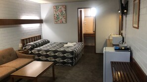 A hotel room with a bed, a sofa, a small table, a desk, and a mirror.